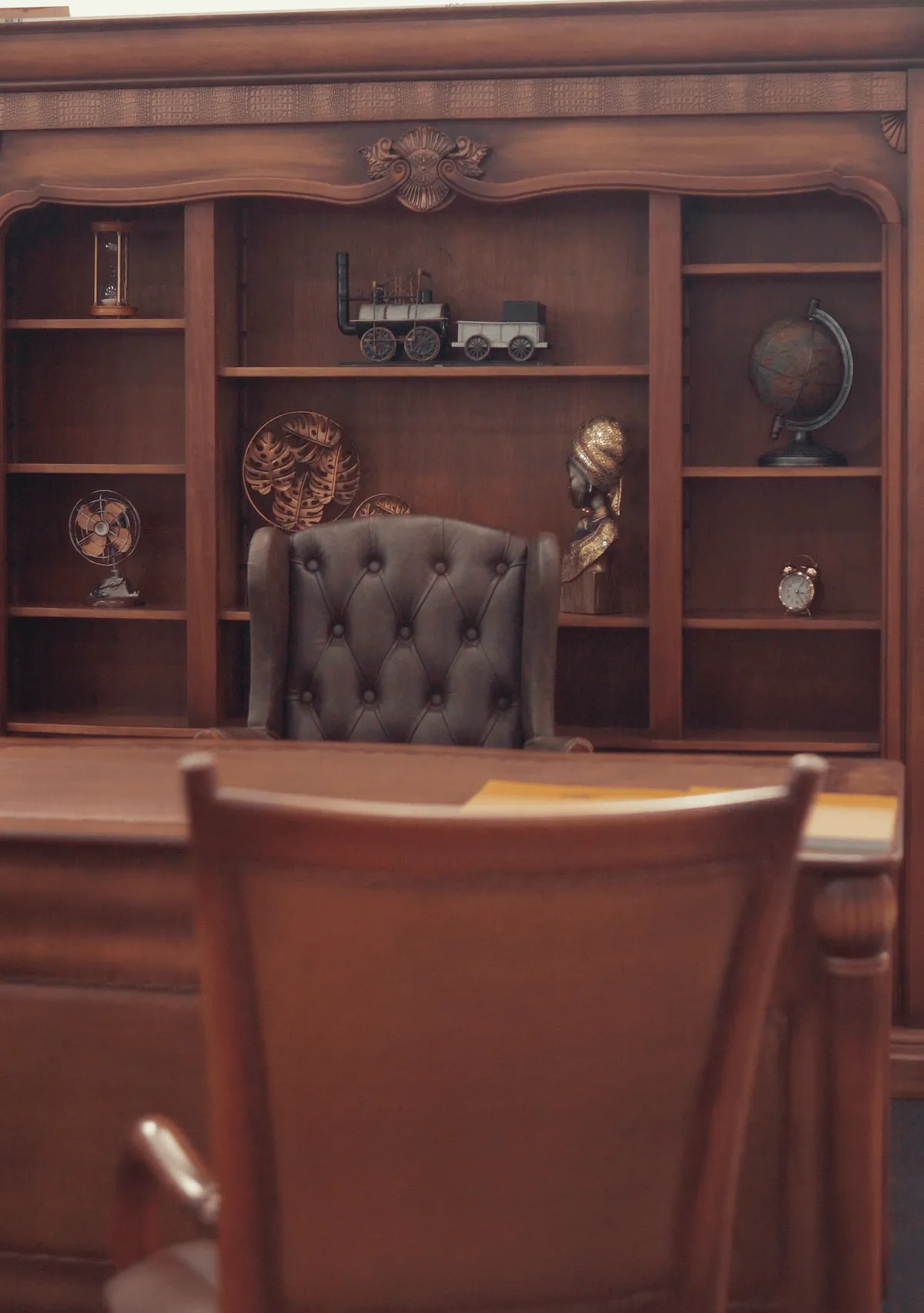 Estante entalhada com poltrona de couro capitonê e objetos decorativos